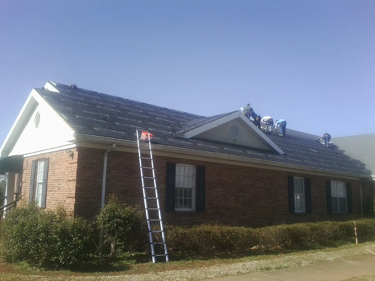 Crew tearing shingles off a brick ranch roof with a ladder set — Emergency Roof Repair work by our crew in Oslo