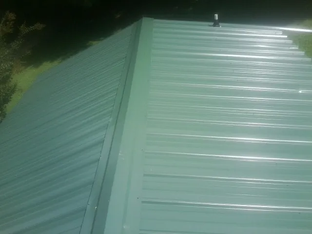 New green metal panels meeting at the ridge of a roof — Flat Roof Repair work by our crew in Oslo