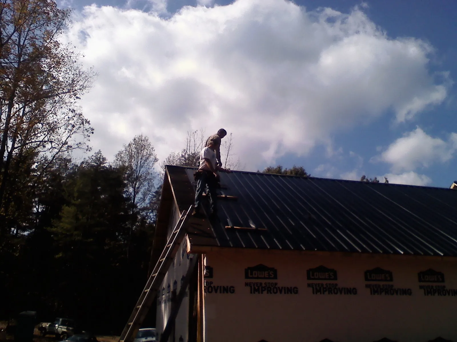 Roofer fastening dark metal panels high against a cloudy sky, from a Roof Inspection job in Oslo